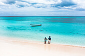 Mann und Frau halten sich an einem tropischen Strand die Hände und bewundern das kristallklare Meer, Luftaufnahme, Antigua und Barbuda, Westindien, Karibik, Mittelamerika
