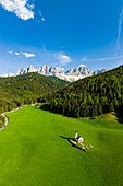 Green forest and meadows surrounding the small Ranui church and Odle in spring, aerial view, Funes Valley, Dolomites, South Tyrol, Italy, Europe