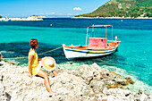 Woman sitting on rocks looking at boats in the turquoise sea, Porto Atheras, Kefalonia, Ionian Islands, Greek Islands, Greece, Europe