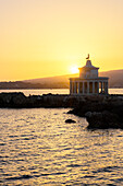 Romantischer Sonnenuntergang über dem Leuchtturm Saint Theodore, der sich im Meer spiegelt, Argostoli, Kefalonia, Ionische Inseln, Griechische Inseln, Griechenland, Europa