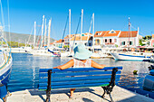 Unbekümmerte Frau entspannt sich auf einer Bank im kleinen Hafen von Fiskardo, Kefalonia, Ionische Inseln, Griechische Inseln, Griechenland, Europa