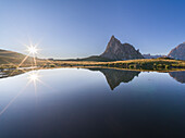 Ra Gusela mountain at Passo Giau and the sun starbeam perfectly reflected in an alpine lake, Dolomites, Italy, Europe