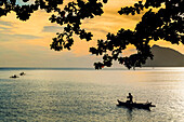 Fishermen paddle outrigger canoes at sunset off Kalea Beach, Kalea, Siau Island, Sangihe Archipelago, North Sulawesi, Indonesia, Southeast Asia, Asia