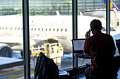 Businessman talking on mobile phone while working on laptop at the airport, Norway, Scandinavia, Europe