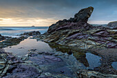 Lila gefärbte Felsen an der Küste Cornwalls bei Sonnenuntergang, Polzeath, Cornwall, England, Vereinigtes Königreich, Europa