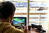Fotograf mit Laptop und Smartphone bei der Planung seiner Fotoreise, Lofoten, Norwegen, Skandinavien, Europa