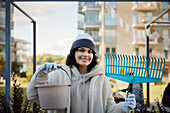 Portrait of smiling teenage girl holding rake and bucket