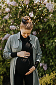 Schwangere Frau berührt ihren Bauch im Freien