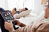 Brothers lying on bed and using phone and tablet
