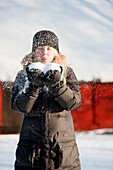 Junge Frau mit einer Handvoll Schnee und pustet hinein