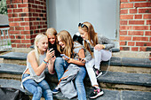 Mädchen, die auf einer Treppe sitzen und ein Mobiltelefon benutzen