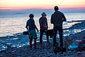 Freunde beim Grillen am Meer bei Sonnenuntergang