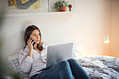 Young woman talking via phone in bed