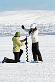 Women drilling hole in ice