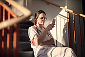 Female doctor sitting on stairs with smartphone