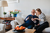 Älterer Mann mit erwachsener Enkelin bei der Nutzung eines digitalen Tablets
