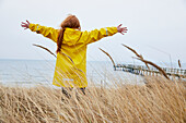 Mädchen in gelbem Regenmantel steht am Meer