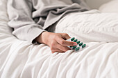 Mann liegt auf dem Bett und hält Tabletten in der Hand