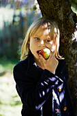Blond girl eating apple in orchard