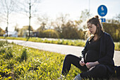 Schwangere Frau am Straßenrand sitzend