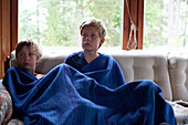 Brothers sitting under blanket on sofa