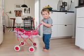 Boy playing with baby carriage in kitchen