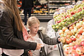Mother and daughter choosing apples in supermarket