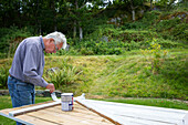 Mann streicht Holztür im Garten
