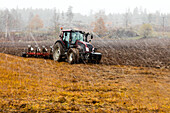 Traktor pflügt Feld bei Regen