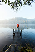 Mann auf Steg im See im Morgennebel