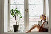 Girl sitting on windowsill with digital tablet