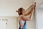 Woman sticking wallpaper on wall