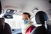 Frau im Auto trägt chirurgische Maske