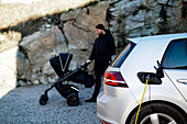 Elektroauto beim Aufladen, Mann mit Kinderwagen im Hintergrund