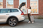 Woman with suitcase standing near car with open boot