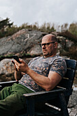 Man on wooden chair using cell phone