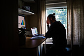 Silhouette of man using laptop at home