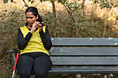 Sehbehinderte Frau sitzt auf einer Bank und benutzt ein Mobiltelefon