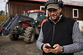 Landwirt mit Mobiltelefon neben dem Traktor