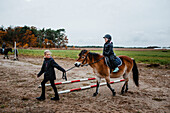Mädchen reitet auf Pony auf der Koppel