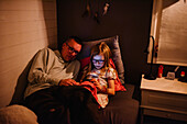 Father with daughter sitting on bed and looking at cell phone
