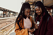 Smiling women using phone at train station platform