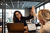 Female coworkers doing high five in cafe