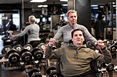 Mann im Rollstuhl trainiert im Fitnessstudio mit Personal Trainer