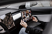 Woman in car holding laptop with video conference
