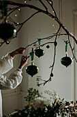 Frau hängt Weihnachtsschmuck an einen Zweig
