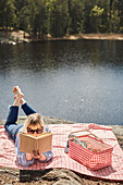 Woman lying on picnic blanket and reading book