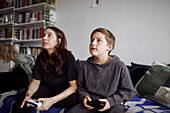 Mother with son sitting on sofa and playing video games