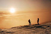 Skiers on snowy slope looking at sunset