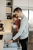 Father carrying toddler girl in kitchen